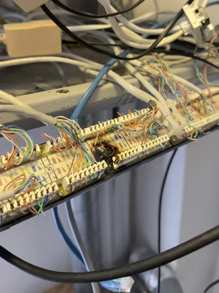 Cable termination panel with a scorched, blackened area and network cables tangled around it