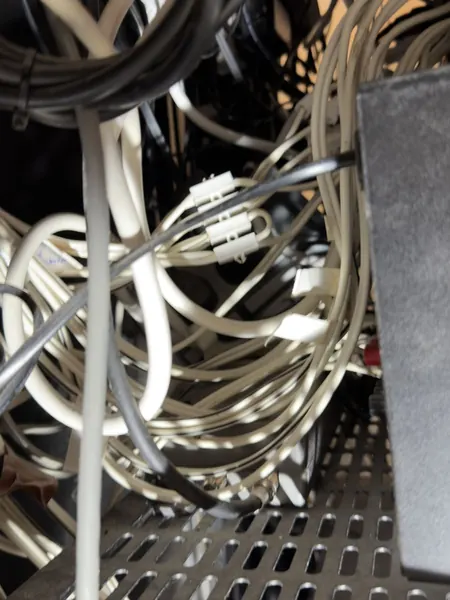 Knot of white, grey and black cables lying across a perforated shelf at the back of the rack