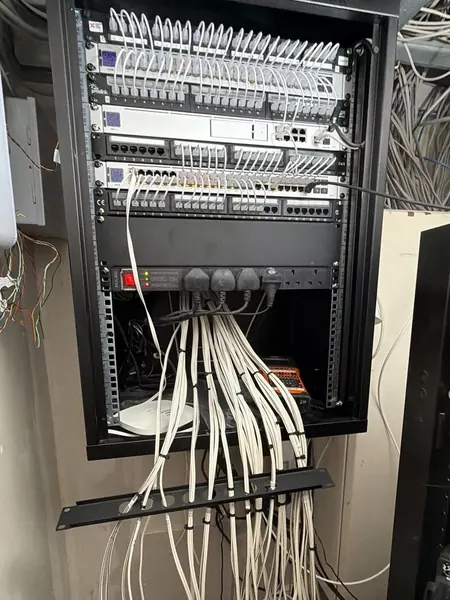Wall cabinet part way through its rebuild, short white patch leads linking panels and switches above a rack power strip, with a label printer at the bottom