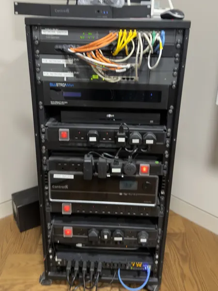 Orange, yellow and white patch leads hang in bunches across the switches of a rack that also holds a Blustream unit and the Control4 units