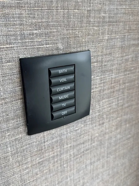 Six button keypad labelled bath, voil, curtain, music, TV and off, against grey woven wallpaper