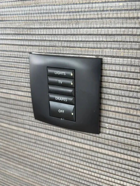 Keypad set into a dark woven wall: four labelled buttons for lights, TV, drapes and off, plus a spare blank one