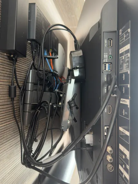 Sockets on the back of the TV, from HDMI to aerial, with a coil of black cable and loose leads draped over the bracket