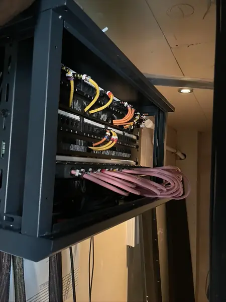Wall mounted second rack with patch panels, yellow and orange leads and pink speaker cables