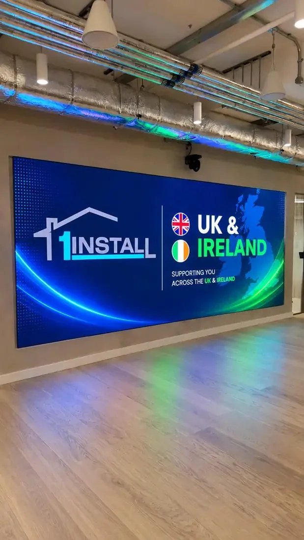 LED video wall in an open office showing the 1Install logo, under exposed ducting and above a pale timber floor