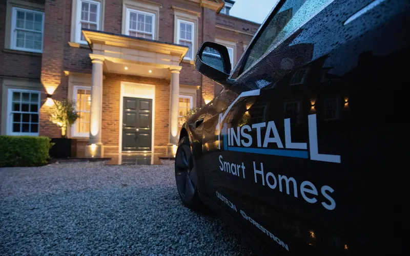 Brick house entrance with a lit portico at dusk and a 1Install branded vehicle in the foreground
