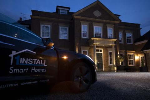 A 1Install Smart Homes car parked outside a large house at dusk