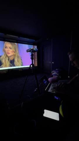 Calibrating a home cinema projector, with a meter facing the screen and an engineer at a laptop