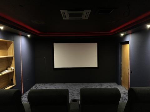 A finished home cinema room with a projection screen, cinema seating and red cove lighting