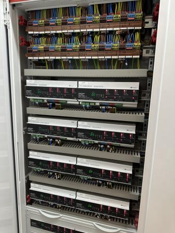 Inside a lighting control panel, with terminal blocks at the top and rows of DIN rail modules below
