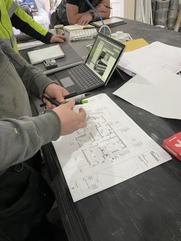 A site meeting around a table, with a marked up floor plan, notebooks and a laptop
