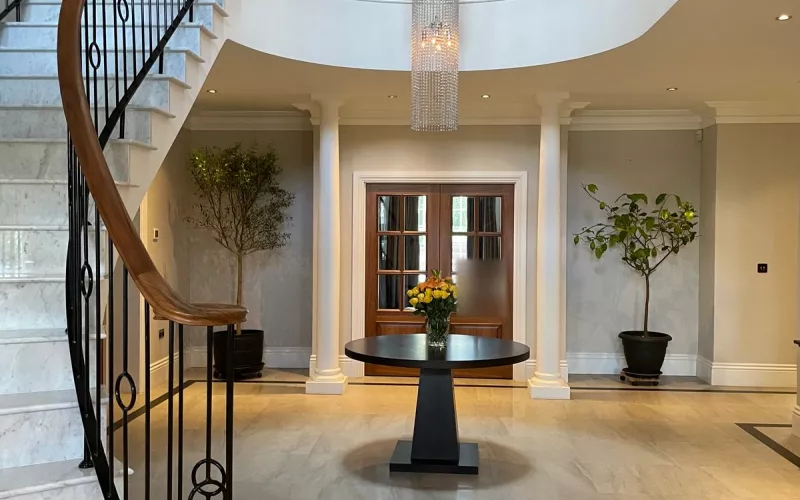 Crestron home automation in a Buckinghamshire house: the entrance hall, with a curved marble staircase, an iron balustrade and a tall crystal chandelier