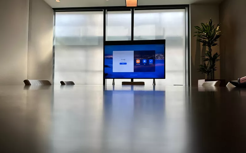 A Neat Board installation seen from down the table: the screen on its castor stand, the dark timber tabletop and daylight from the glazing behind