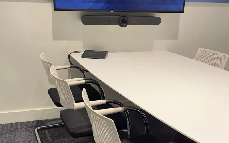 A meeting room video bar from Logitech mounted under the screen, looking out over a white table ringed by white chairs