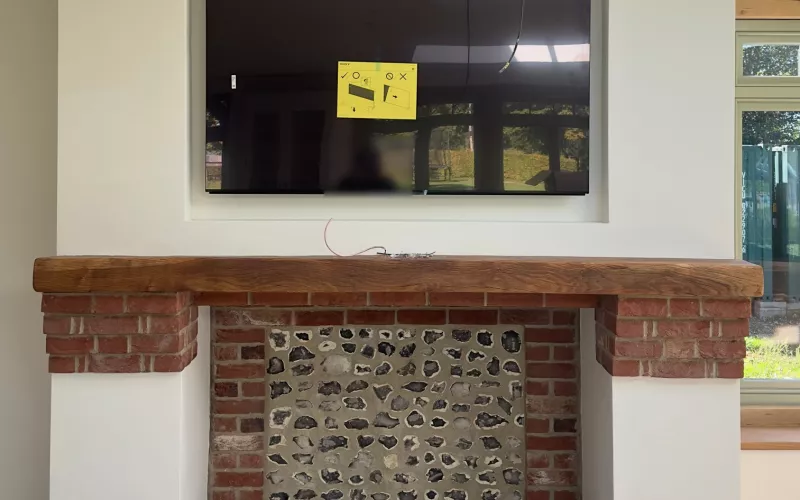 TV installation in Hampshire: a TV set into a recess above an oak beam mantel, with a brick and flint fireplace below