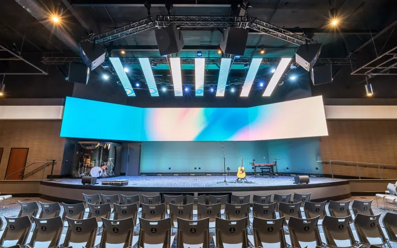 Biamp church audio at River Valley Church: empty sanctuary with grey chairs facing a stage and wide LED screen, Community LVH-900 steerable horns hung from the lighting truss above