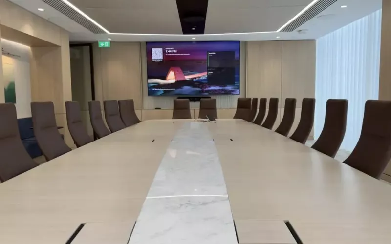 Timber panelled boardroom with a long table, brown leather chairs and a wall display with a video bar beneath it, the size of room where a plan for Google Meet hardware on ChromeOS or Android matters most