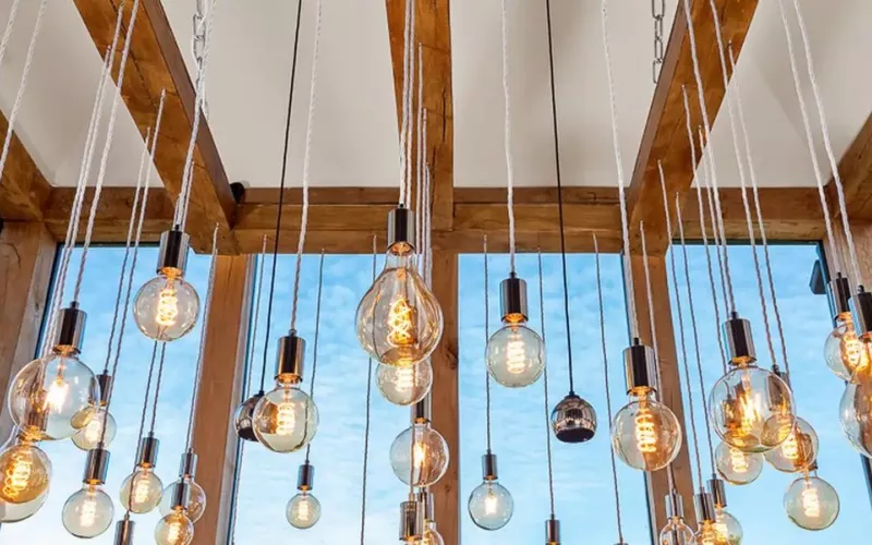Lighting design in a glazed oak frame room: dozens of filament pendants hung at different heights between the beams, with spotlights on the frame