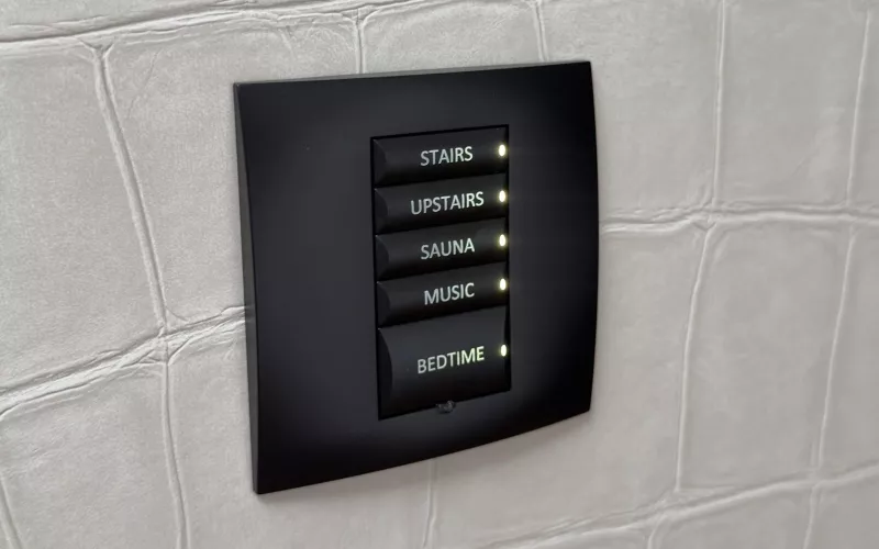 Five backlit buttons on a black wall keypad read stairs, upstairs, sauna, music and bedtime, in the house going from Control4 to Crestron Home