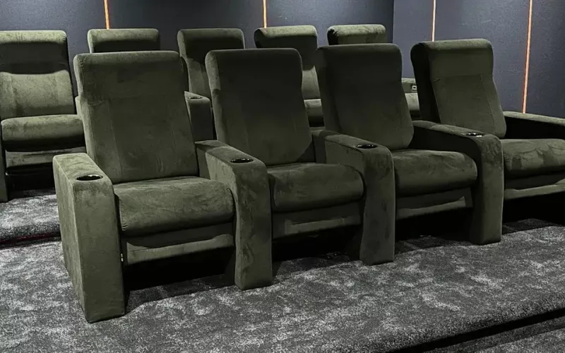 Two tiered rows of dark green velvet recliners on grey carpet in a finished home cinema, the kind of room a Crestron Cevo Mini Remote is made to control