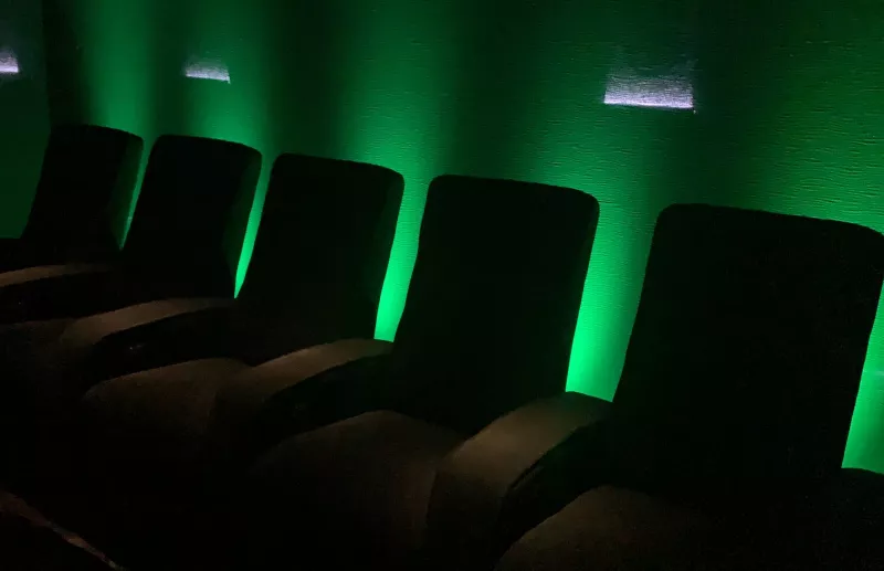 Row of recliners in a Berkshire home cinema with the wall behind them lit green, and small wall lights higher up