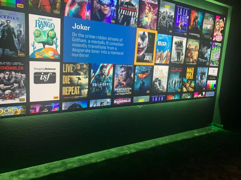 Close view of the cinema screen showing a library of films, with green light along the floor beneath it