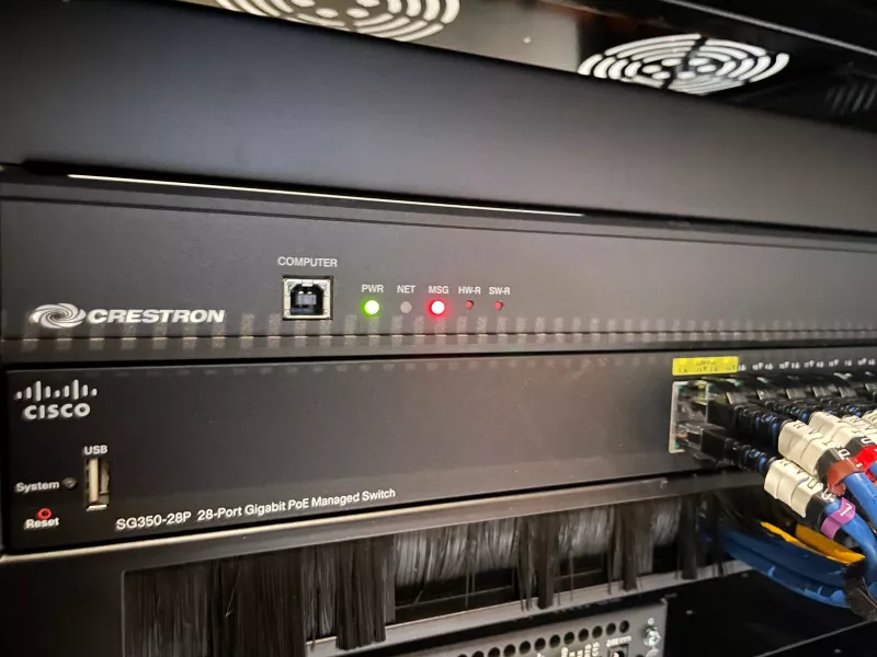 Front of the rack: a Crestron control processor above a Cisco SG350-28P PoE switch, with patch leads plugged in and a brush strip below