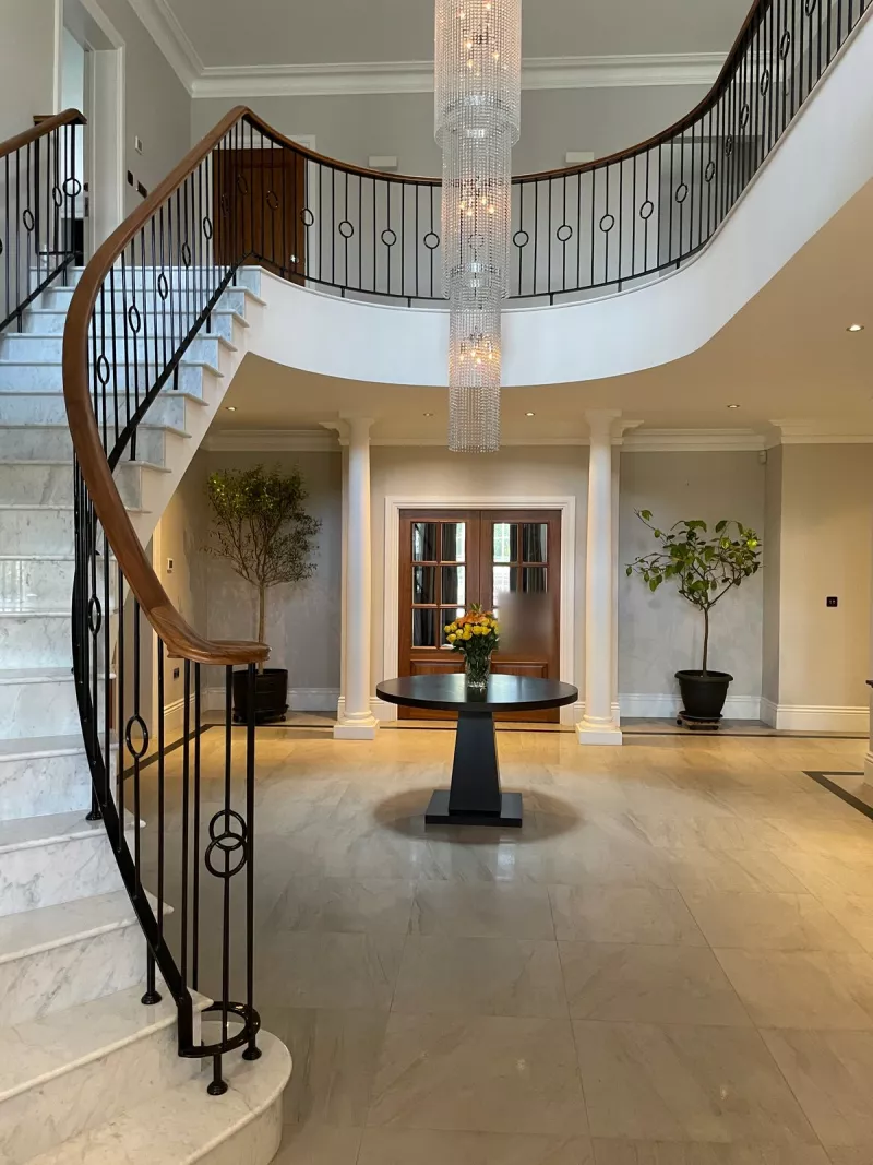 Crestron home automation in a Buckinghamshire house: the entrance hall, with a curved marble staircase, an iron balustrade and a tall crystal chandelier