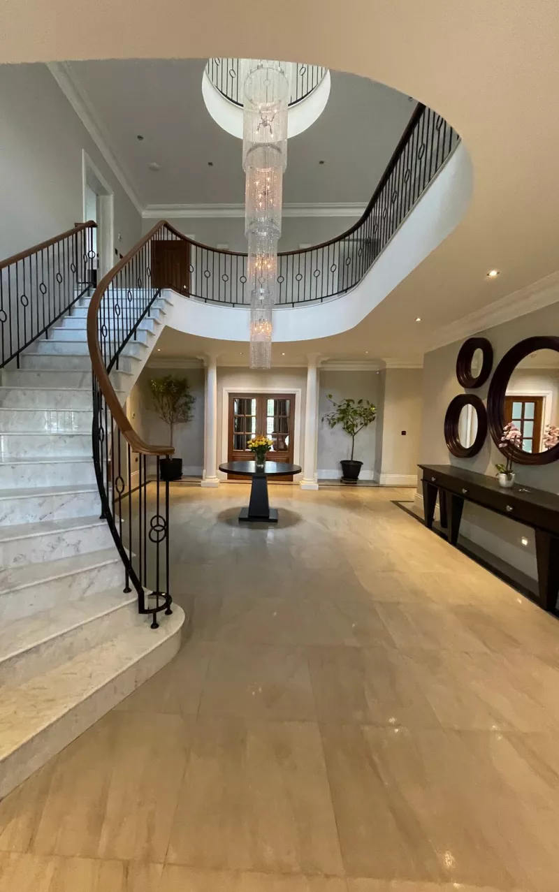 Another view of the hall, with round mirrors above a long console table, the chandelier and glazed doors at the far end