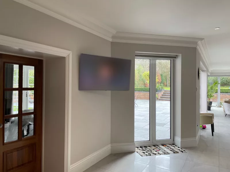 A TV mounted on the wall beside glazed doors to the terrace and garden, with a panelled timber door on the left