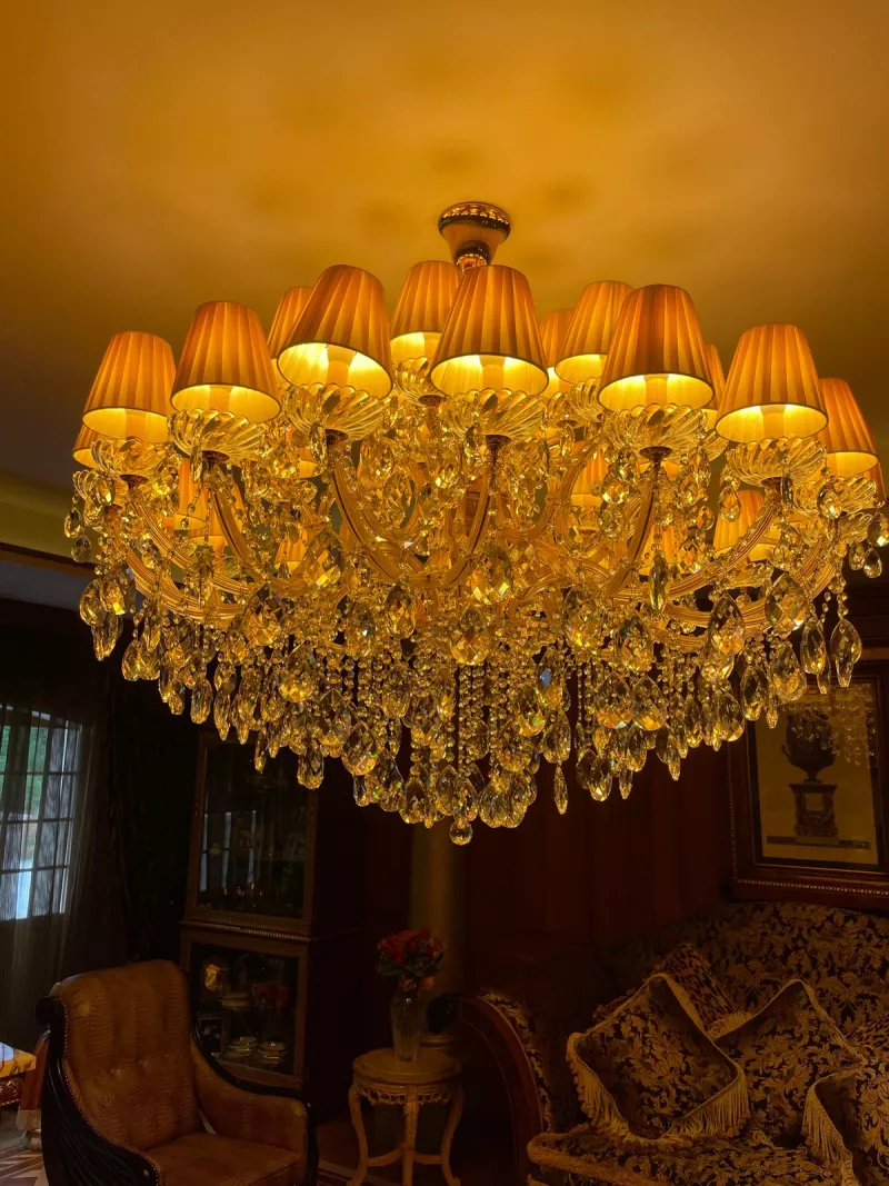 Crystal chandelier with cream pleated shades glowing warm over a Surrey sitting room with dark wood and patterned sofas