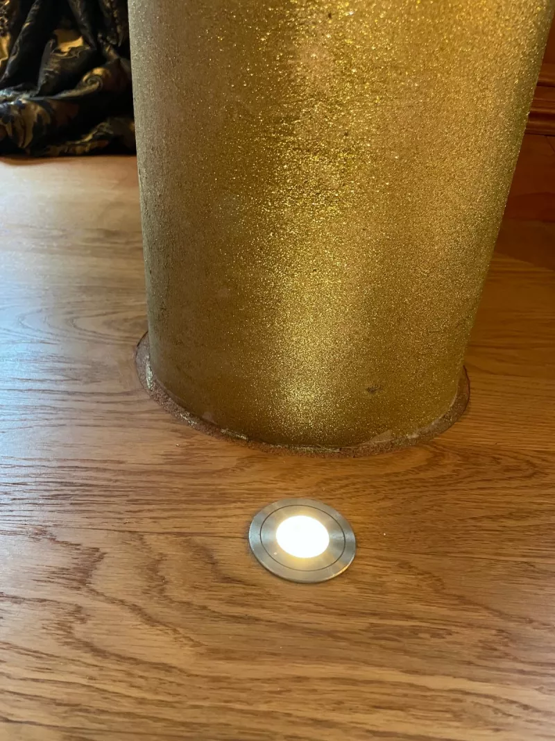 Small round LED set into an oak floor beside a gold glitter column