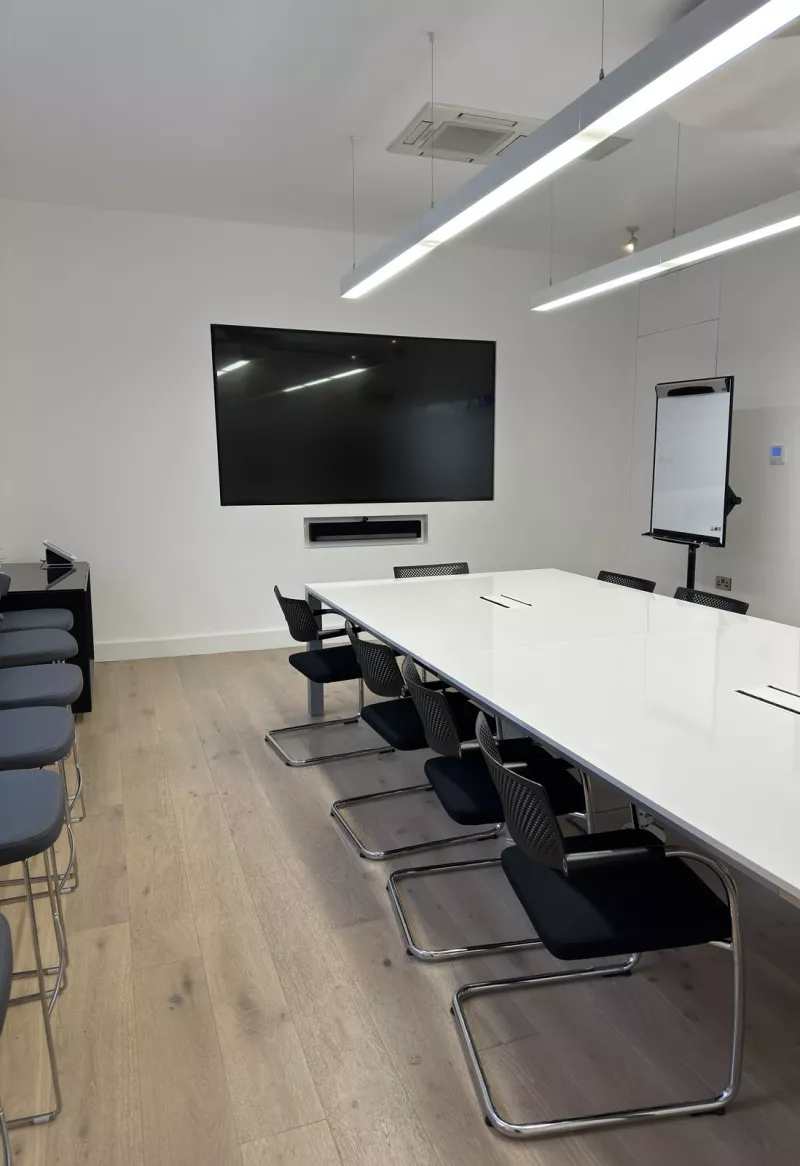 Side view of the meeting room taking in the screen, the soundbar in its recess, the flip chart and the long white table