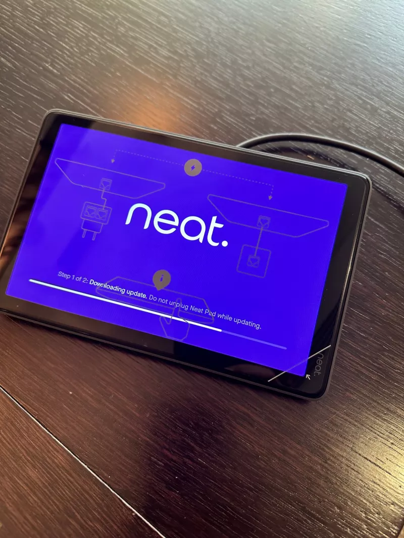 The Neat Pad touch controller on the boardroom table part way through an update, its screen telling people to leave it plugged in