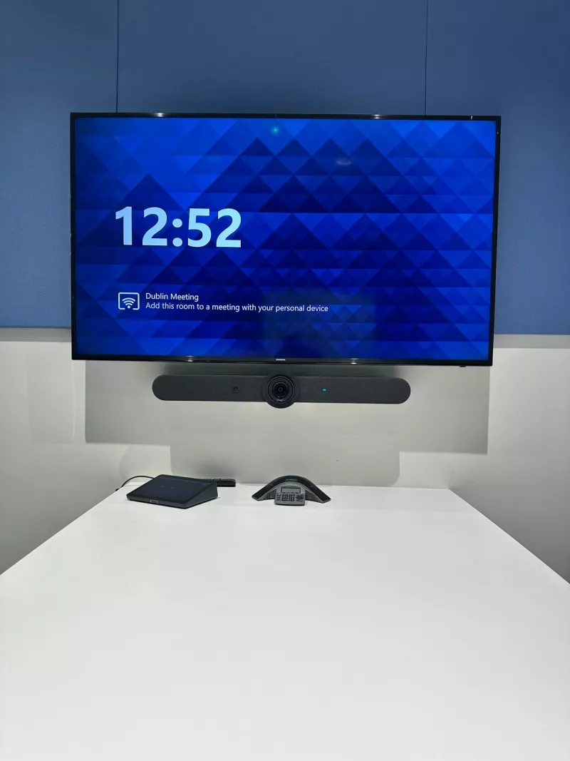 The Samsung screen with the Logitech bar beneath it, and a Logitech Tap and a conference speakerphone waiting on the table