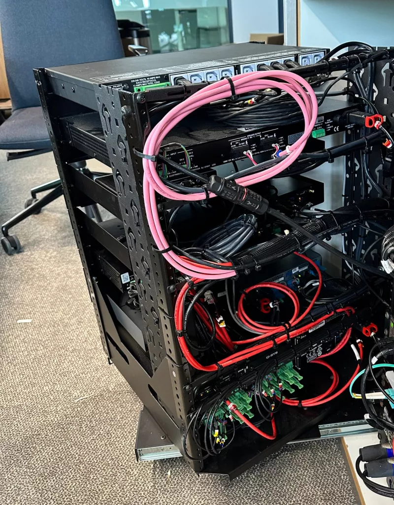 Behind the rack, pink cables coiled and tied, red wires into green terminal blocks and a row of power sockets across the top