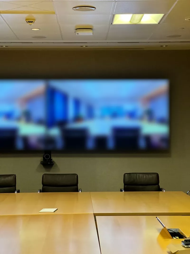 Facing the end wall head on: the two screens edge to edge, the camera bracket below them and the chairs at the head of the table