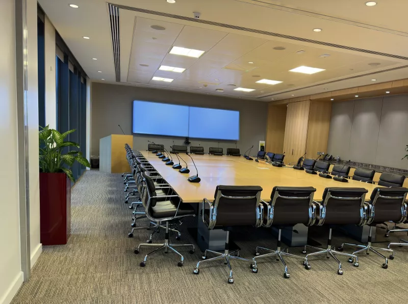 Looking in from the doorway: rows of black leather chairs, a lectern with a gooseneck microphone and two displays on the end wall