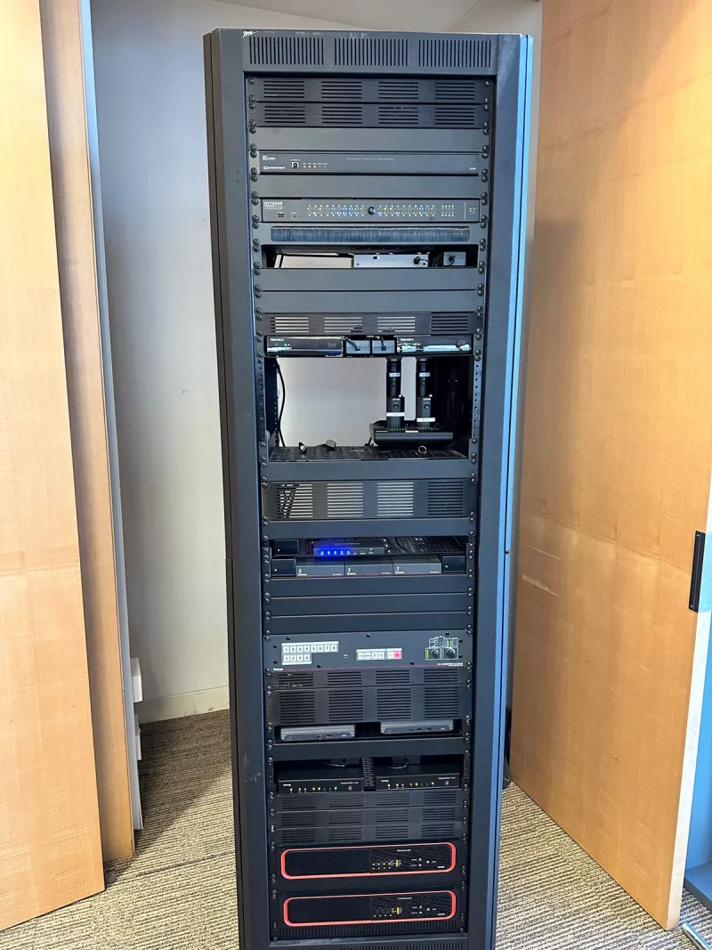 The equipment rack between timber doors, running from Crestron control at the top through Shure wireless microphones on a shelf to two Biamp amplifiers at the base