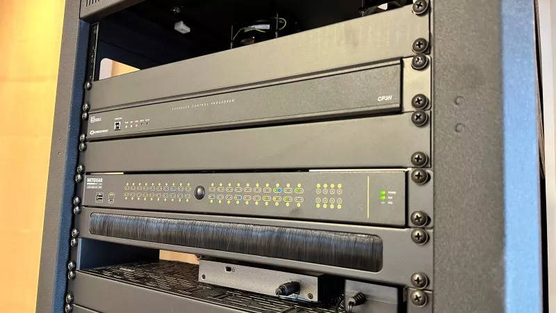Close view of a Crestron CP3N processor with a Netgear AV Line switch below it and a brush strip underneath