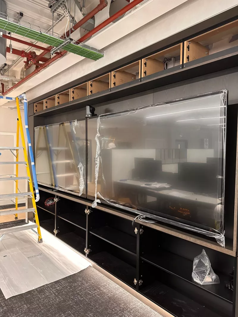 Two large displays in protective film in a joinery wall with a camera above them in a London office fit-out