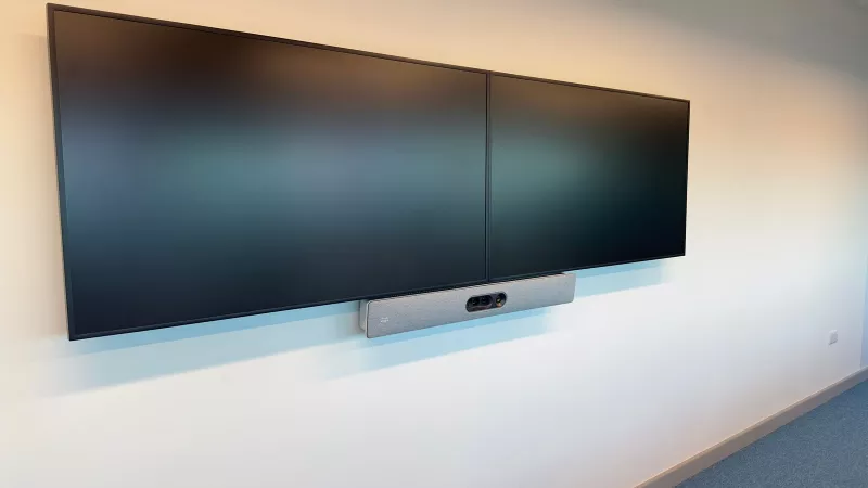 A pair of displays on a white wall with the grey Cisco bar fitted centrally beneath them
