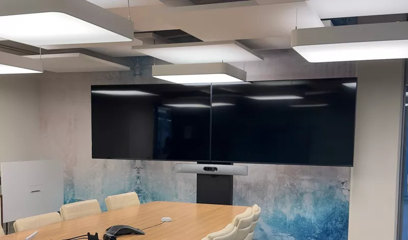 Two large screens on a floor stand at the end of a boardroom, the Cisco bar fixed to the stand below them and cream chairs around the timber table