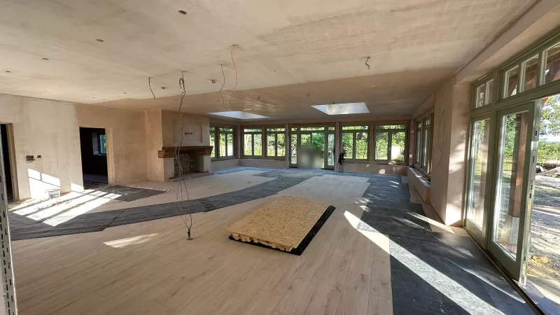 Unfinished room in a Hampshire new build in July 2025, with boarded ceilings, floor protection, a fireplace at the far end and cables hanging from the ceiling