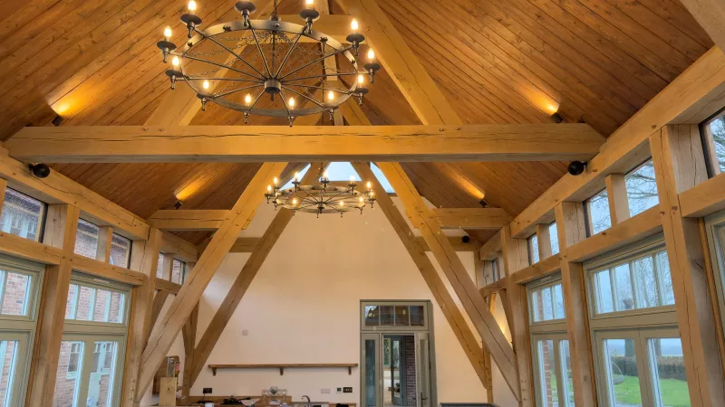 Finished oak frame room in a Hampshire new build with a vaulted pine ceiling, two wheel chandeliers and warm light on the timber