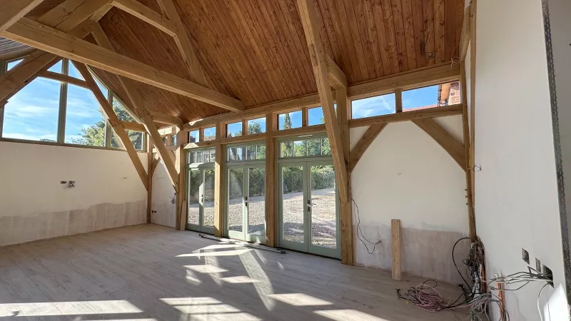 Oak frame room in a Hampshire new build before finishing, with a bundle of cables and copper pipework at the foot of a wall