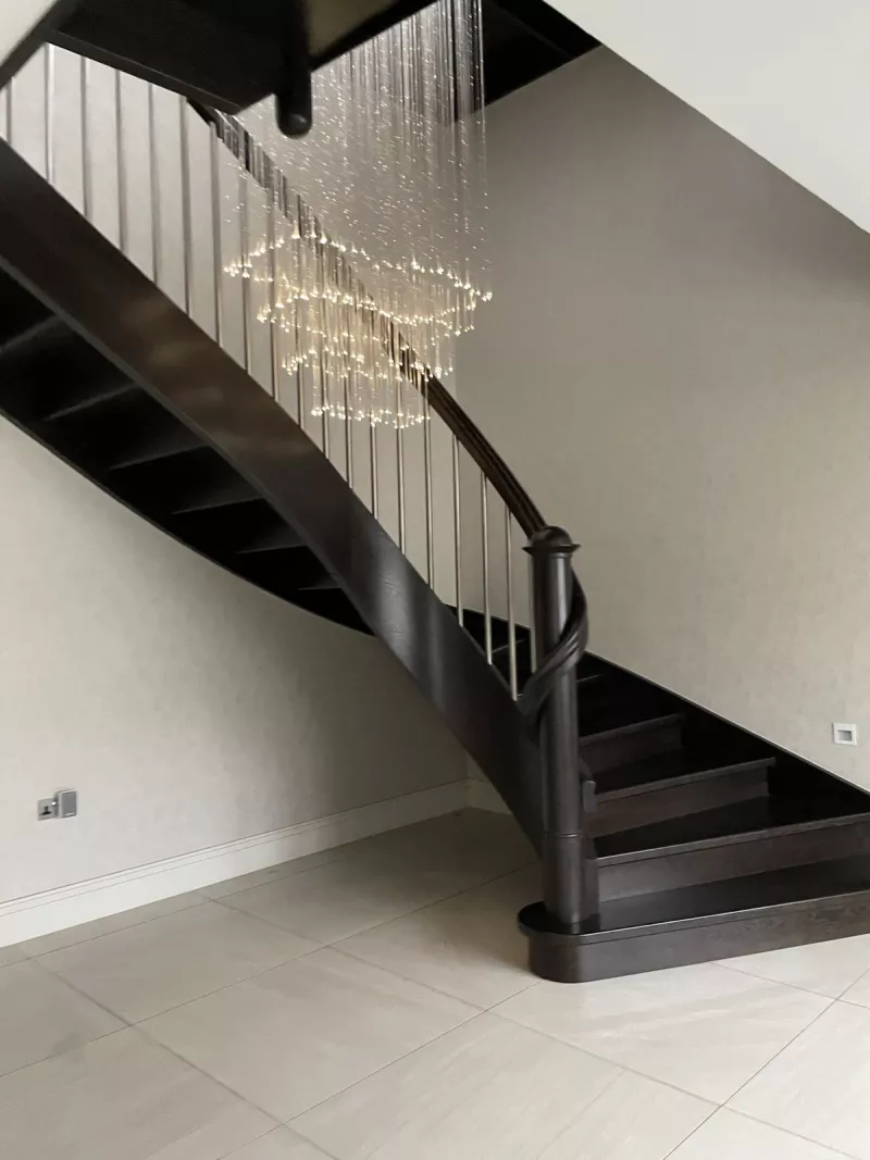 Curved dark wood staircase with a cascading chandelier