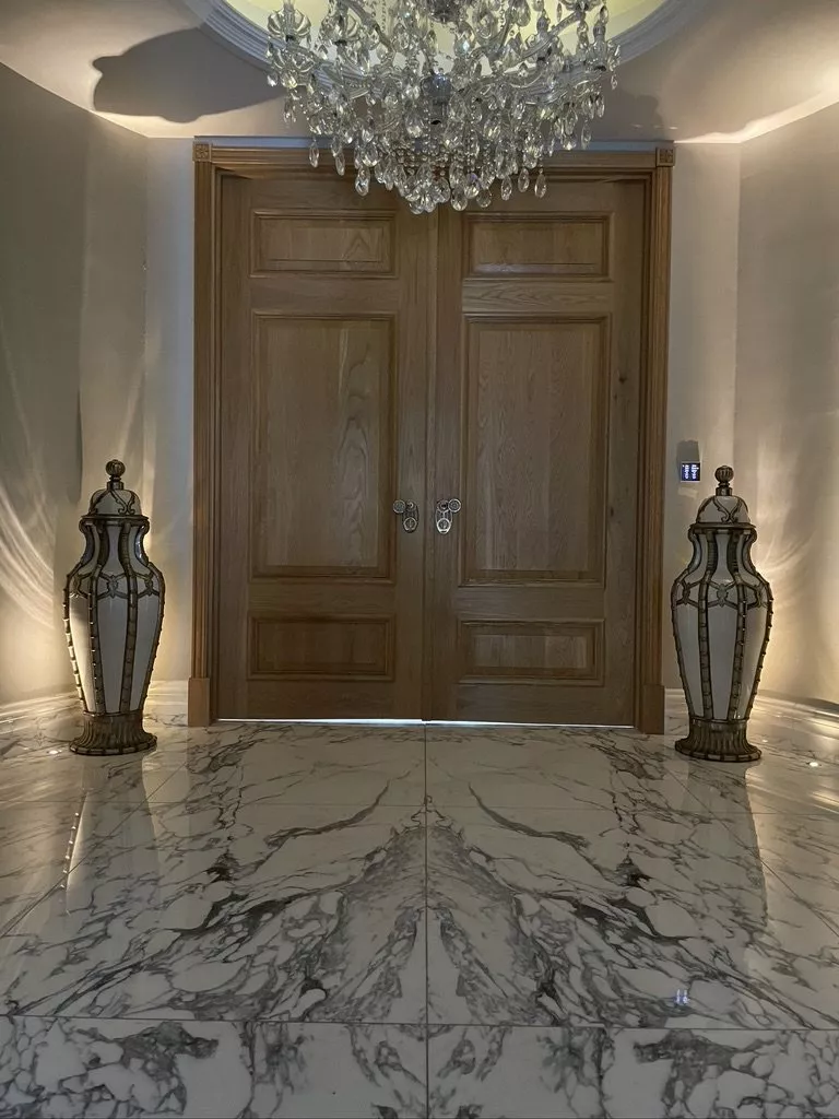 Oak double doors and a marble floor lit by uplighters and a crystal chandelier, a hallway where a KNX installer in Surrey sets the welcome scene