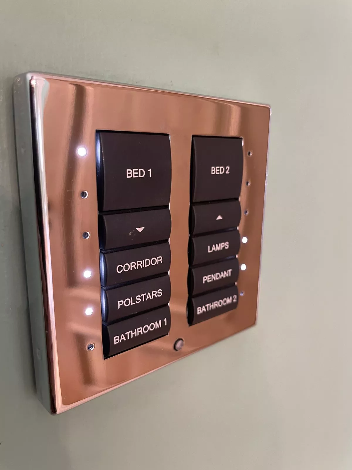 Rose gold wall keypad on a pale wall with backlit buttons for the bedrooms, corridor, lamps and pendant, the kind of control 1Home KNX also puts on your phone