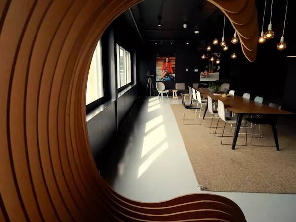 A meeting space with a long table, white chairs and pendant lights